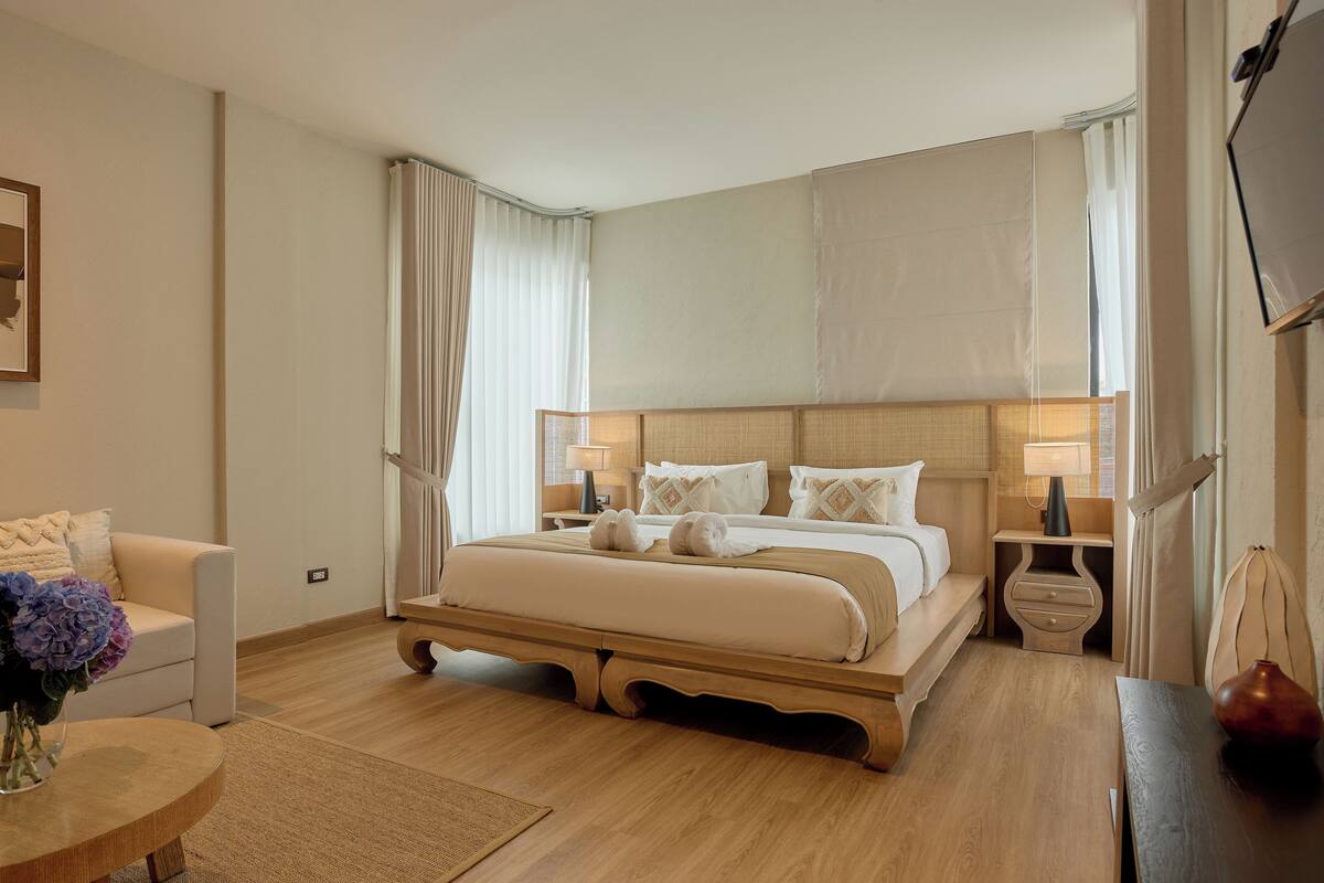 Una habitación de hotel moderna con una cama grande, mesitas de noche, un televisor y una zona de estar con una mesa y sillas.