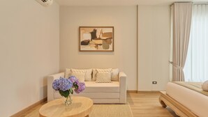 Habitación de hotel moderna con un sofá color crema, una mesa redonda de madera con un florero, y un cuadro en la pared.