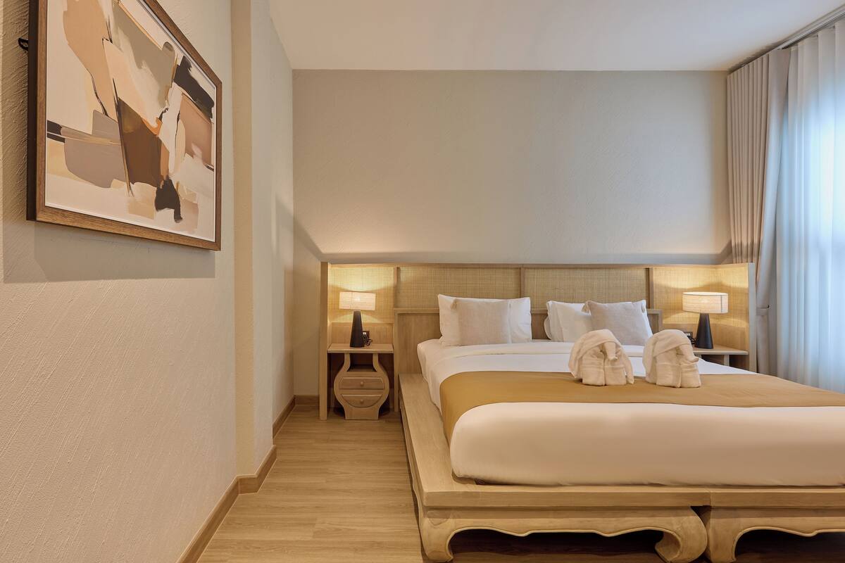 Una habitación de hotel con una cama grande, dos mesitas de noche con lámparas, un cuadro en la pared y una ventana con cortinas.