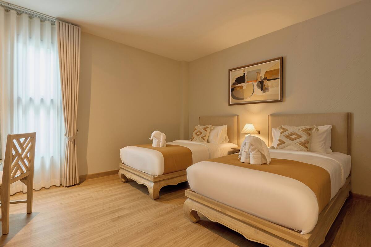 Habitación de hotel con dos camas, una silla de madera y un cuadro en la pared.