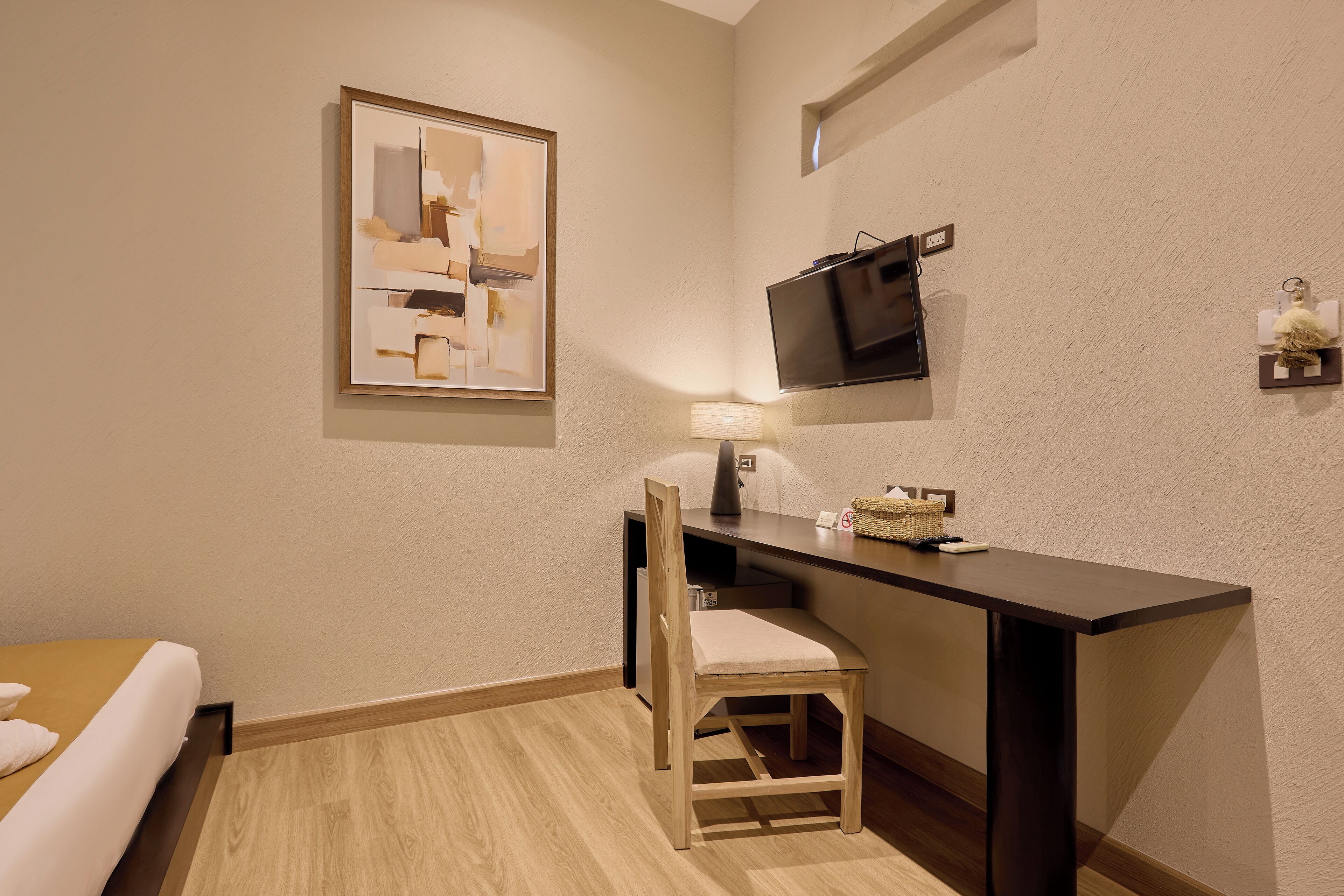 Ein Hotelzimmer mit einem Bett, einem Schreibtisch mit Stuhl, einem Fernseher und einem gerahmten abstrakten Gemälde an der Wand.