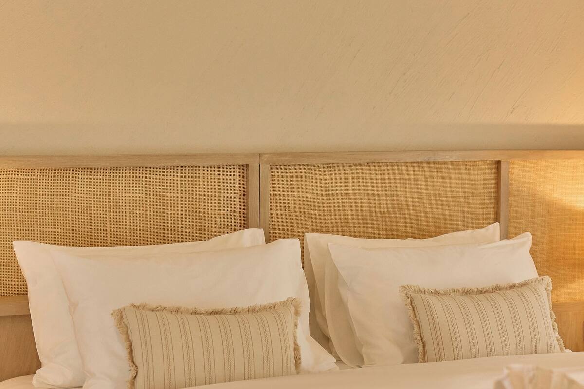 Una cama bien hecha con sábanas blancas y un plaid marrón, un cabecero de madera y una toalla doblada sobre la cama.