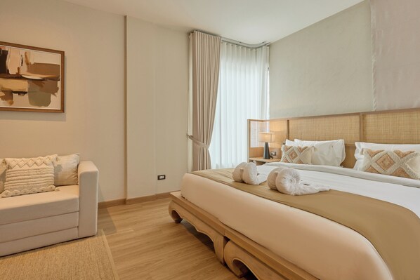 Habitación de hotel con una cama grande, un sofá, un cuadro y una ventana con cortinas.