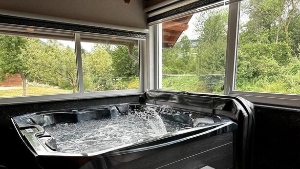 A hot tub with water flowing, positioned near large windows with a view of greenery outside. - Rijeka Villa-Spacious 4BR with Pool (East Sarajevo)