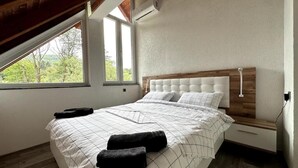 A bedroom with a large bed, a wooden headboard, and a window providing a view of trees. - Rijeka Villa-Spacious 4BR with Pool (East Sarajevo)