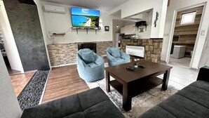 A modern living room with a fireplace, two blue armchairs, a dark coffee table, and a TV mounted on the wall. - Rijeka Villa-Spacious 4BR with Pool (East Sarajevo)