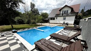 A swimming pool with checkered flooring, wooden lounge chairs, and a house in the background. - Rijeka Villa-Spacious 4BR with Pool (East Sarajevo)