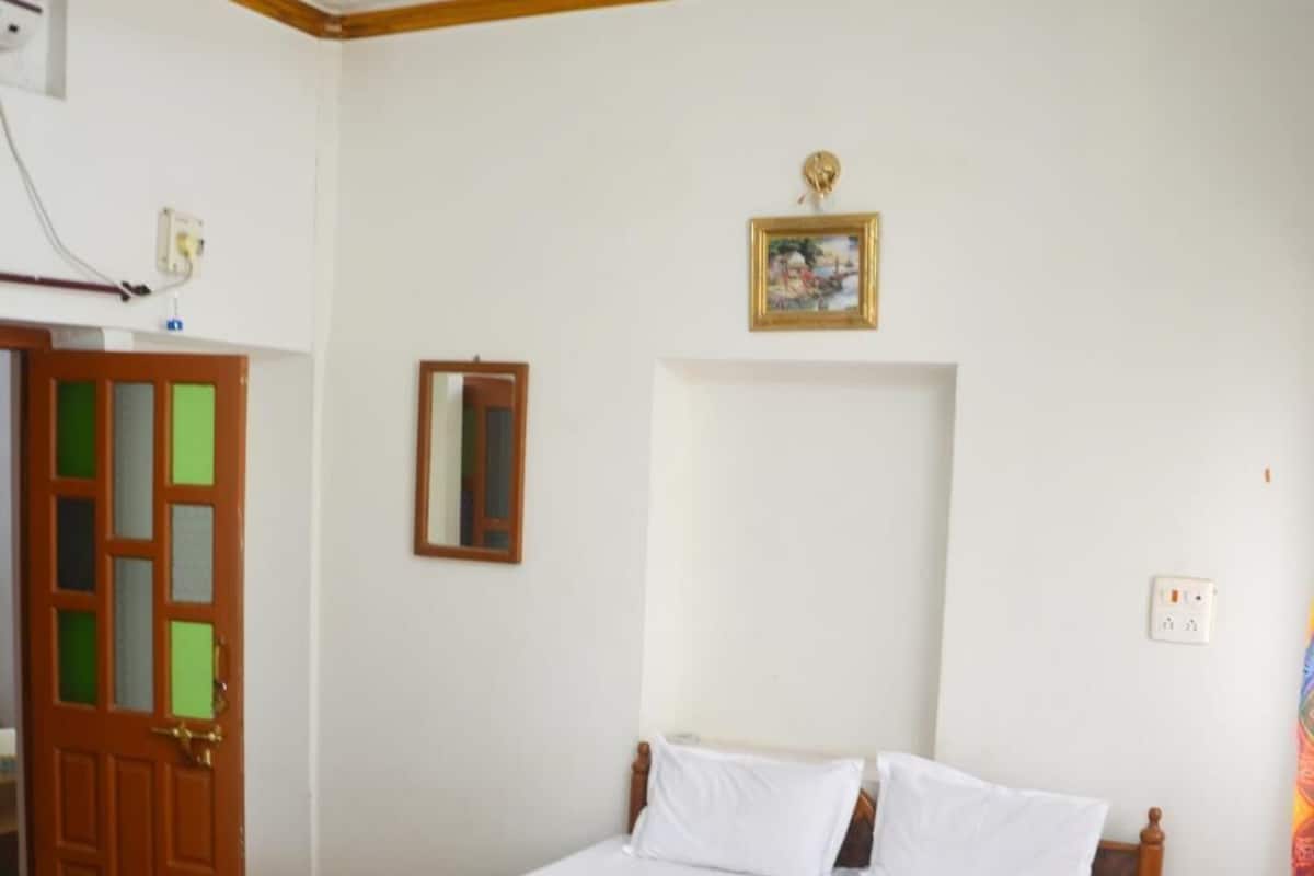 A bedroom with a wooden bed, white linens, a ceiling fan, a door with glass panels, and a framed picture on the wall.