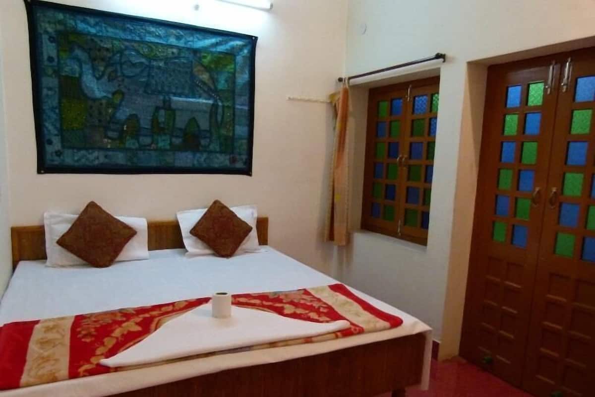 A hotel room with a bed, a painting, a window with a curtain, and a wooden door.