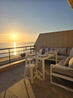 A terrace with a table set for two, overlooking a sunset over the sea. - Azulmaris - Right on the beach | Terrace & ocean view (Vila do Conde)