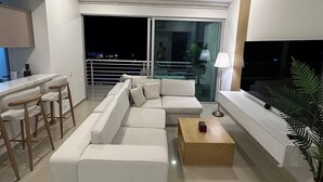 A modern living room with a sectional sofa, a wooden coffee table, a TV mounted on the wall, and a balcony with a view of the city at night. - Lujoso apartamento Rodadero. .. 3 min playa (El Rodadero)