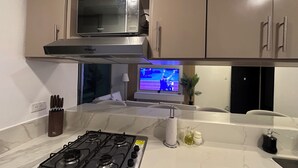 A modern kitchen with a gas stove, a microwave, and a TV displaying a sports event.