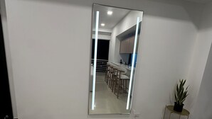 A modern, minimalist room with a large mirror reflecting a kitchen area.