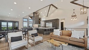 Un salon moderne avec un canapé, des fauteuils et une table basse. Il y a un coin cuisine avec des placards et un coin repas avec des chaises.