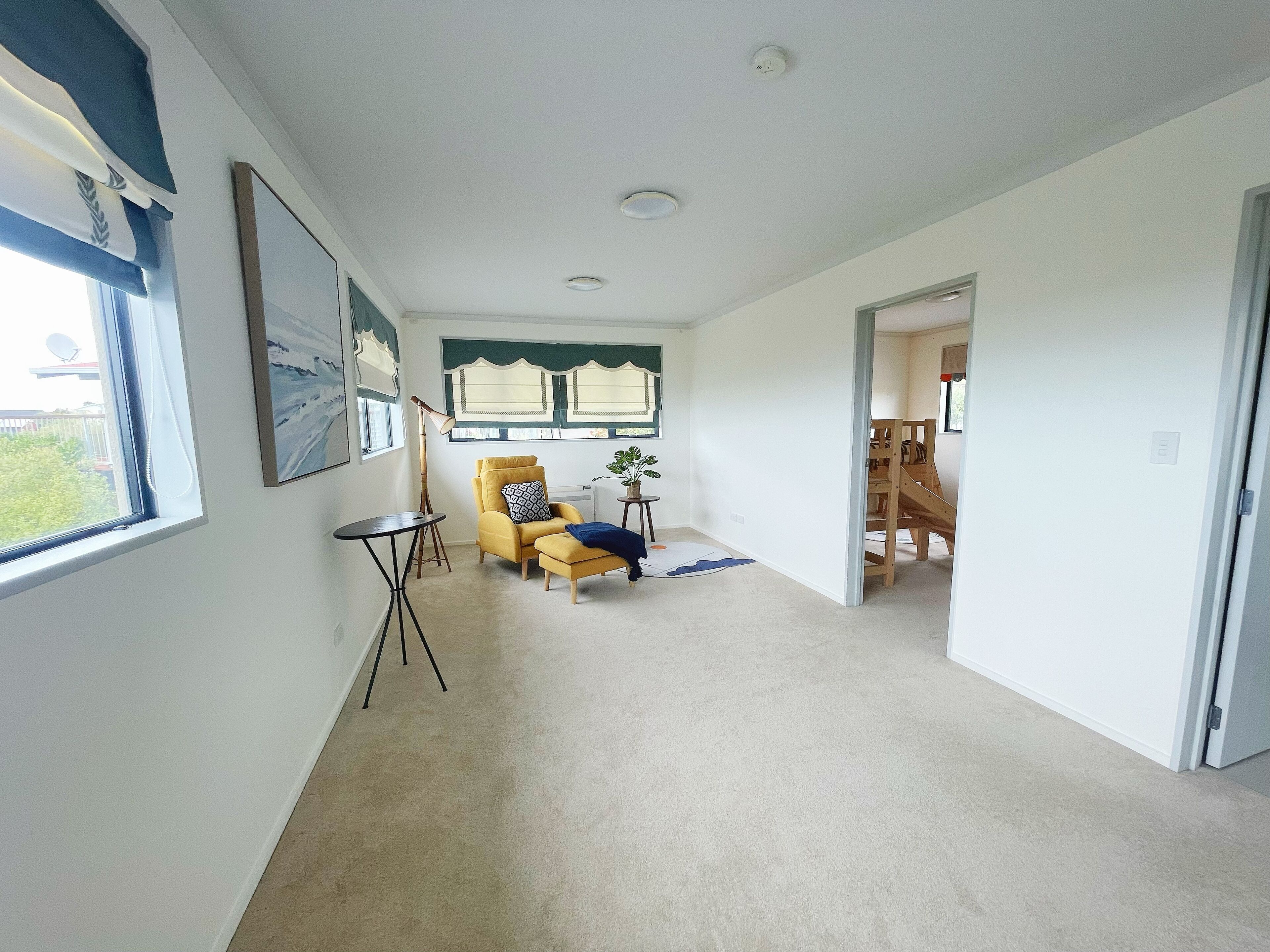 Un hall d’entrée spacieux, avec un fauteuil jaune, une petite table et une plante en pot.