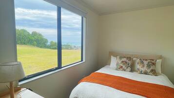 Ein Schlafzimmer mit großem Fenster, einem Bett mit orangefarbener Decke und einem Schreibtisch mit Lampe.