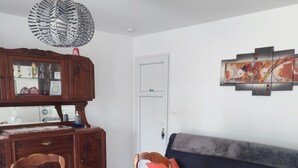 Ein Essbereich mit rundem Tisch, Holzsesseln, Deckenventilator, einer Vitrine und einer Couch mit Kissen.
