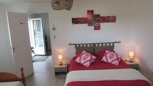 Ein Schlafzimmer mit einem Bett, zwei Nachttischen mit Lampen, einem hölzernen Kopfteil, einer rot-weißen Bettdecke und einem modernen, abstrakten Wandbild.