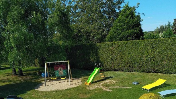 Ein gepflegter Garten mit Kinderspielbereich, einschließlich Schaukel und Rutsche. Es gibt Außenbereiche mit Sitzgelegenheiten, Stühlen und einem Tisch.
