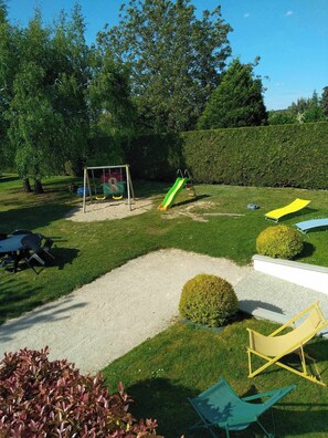 A well-maintained garden with a children's play area, including a swing set and a slide. There are outdoor seating areas with chairs and a table.