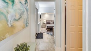A hallway with a large abstract painting, a bed with a 'RELAX' pillow, and a door leading to another room. - Extended-Stay Suite Near I-15 in Lake Elsinore! (Lake Elsinore)