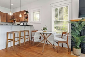 Une cuisine avec des meubles de rangement en bois, une table ronde en verre et deux tabourets en bois.