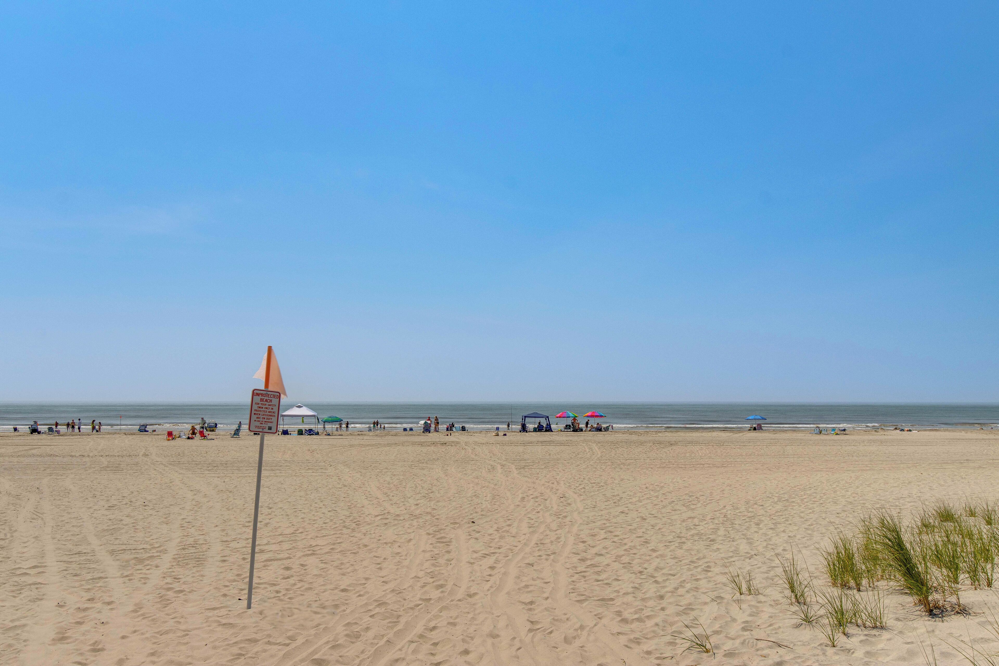 Une vaste plage de sable, avec un drapeau de surveillance, des parasols et des gens.