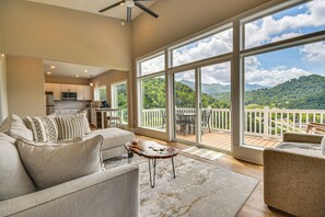 A spacious living room with a large window offering a mountain view, a cozy seating area with a coffee table, and a kitchen in the background. - Cozy 2BR/2BA Mtn Escape w/ views in Maggie Valley (Maggie Valley)