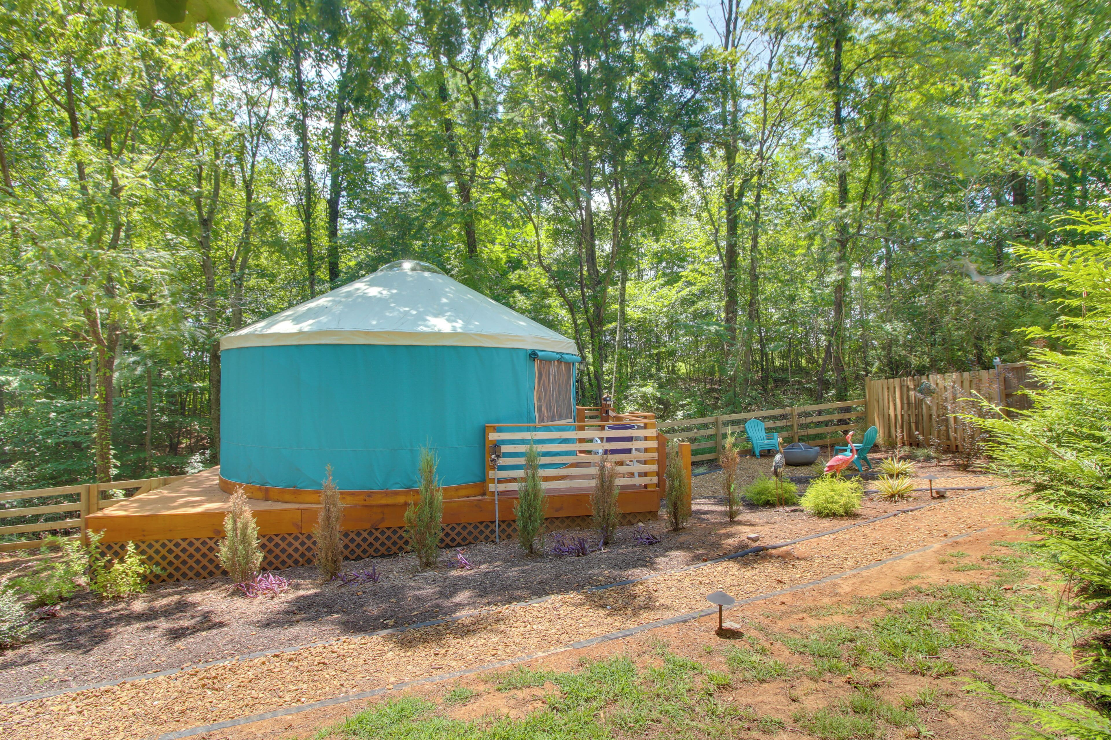 A yurt with a wooden deck and a fenced area with plants and a bird statue.