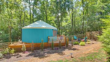 A yurt with a wooden deck and a fenced area with plants and a bird statue.