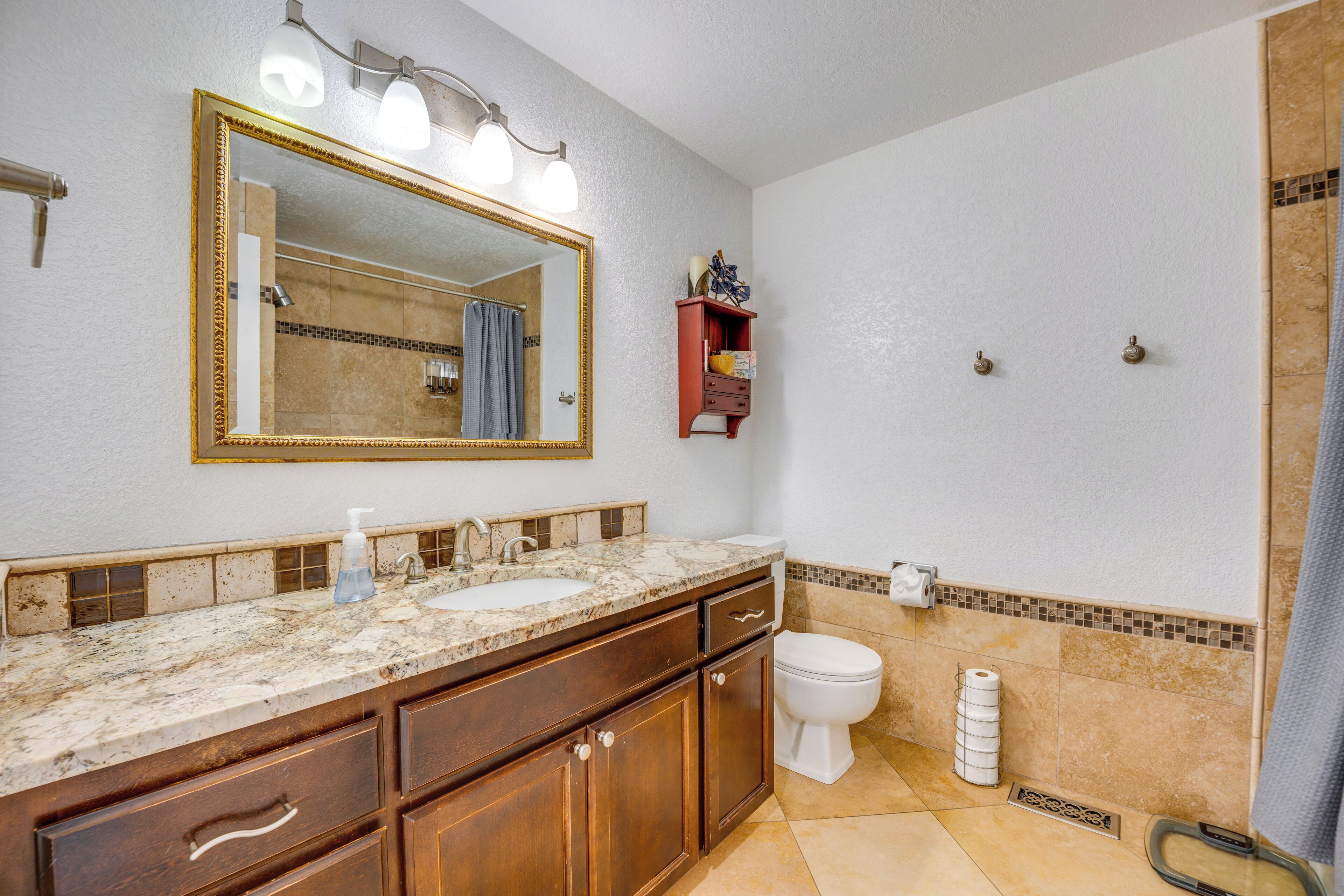 Une salle de bain comprenant un meuble-lavabo à deux vasques, des toilettes, un espace douche et un miroir avec éclairage intégré.