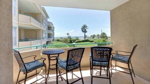A balcony with a table and chairs, overlooking a residential area with a view of the ocean and palm trees. - Ocean Pearl= pool,  beachfront, elevator (Tybee Island)