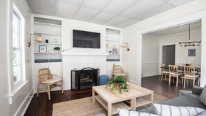 A living room with a fireplace, a television mounted above it, and a dining area with chairs and a table. - Tri-City Traditions – Groups/WiFi/Downtown (Birmingham)