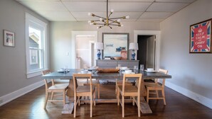 A dining room with a rectangular table, six wooden chairs, a chandelier, and a painting on the wall. - Tri-City Terrace – 3 Units/Groups/Games/Fun (Birmingham)