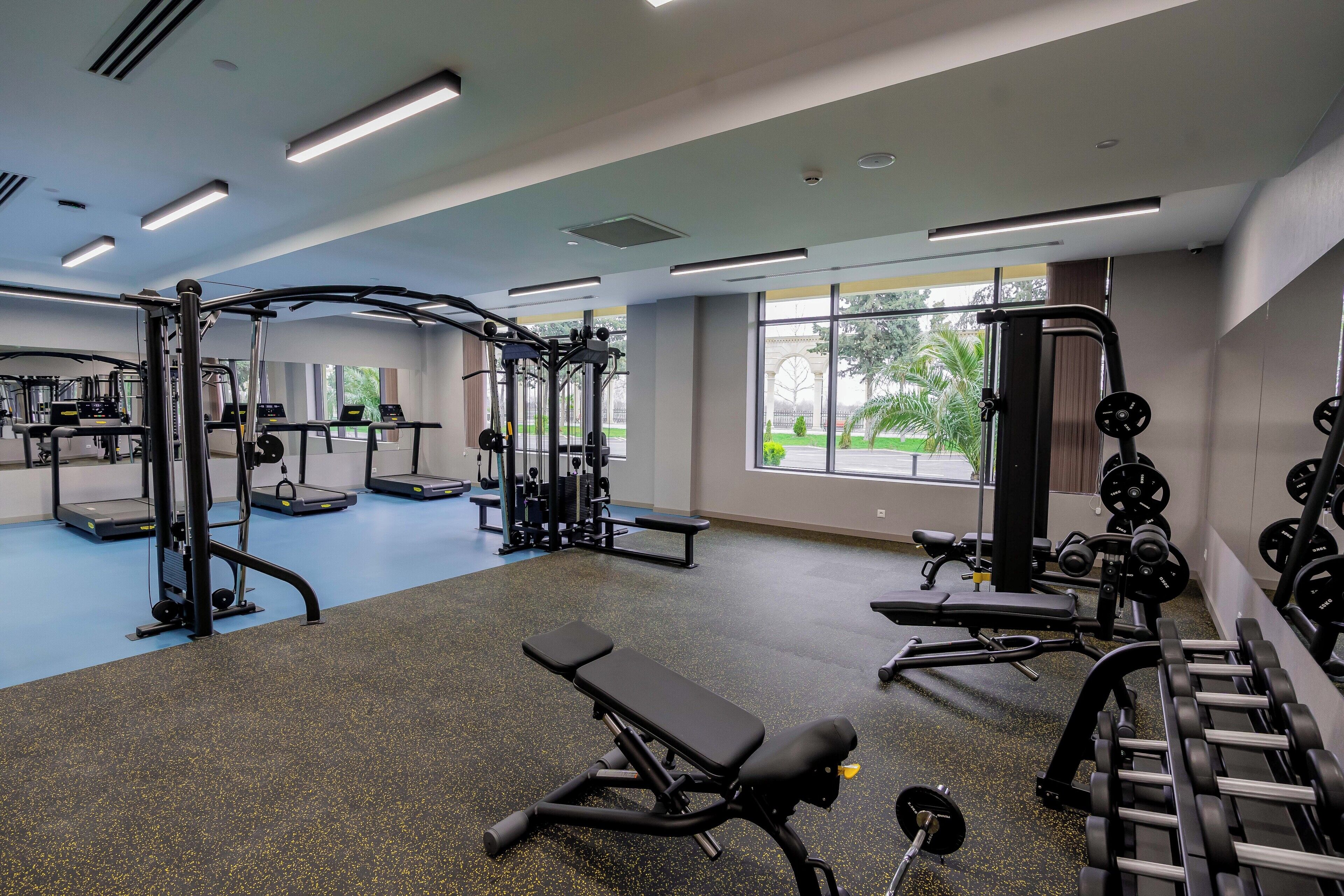 A gym with exercise equipment, benches, and a view of greenery outside.