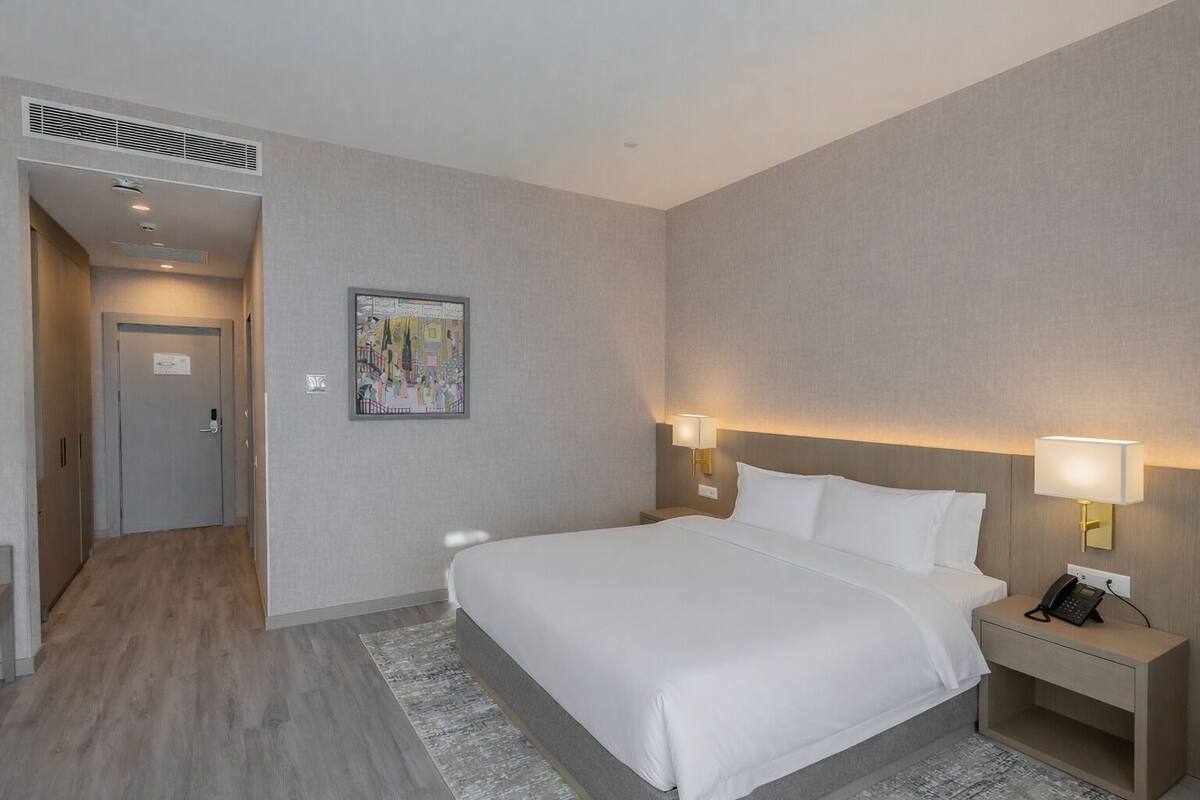 Een hotelkamer met een bed, nachtlampjes, een telefoon en een schilderij aan de muur.
