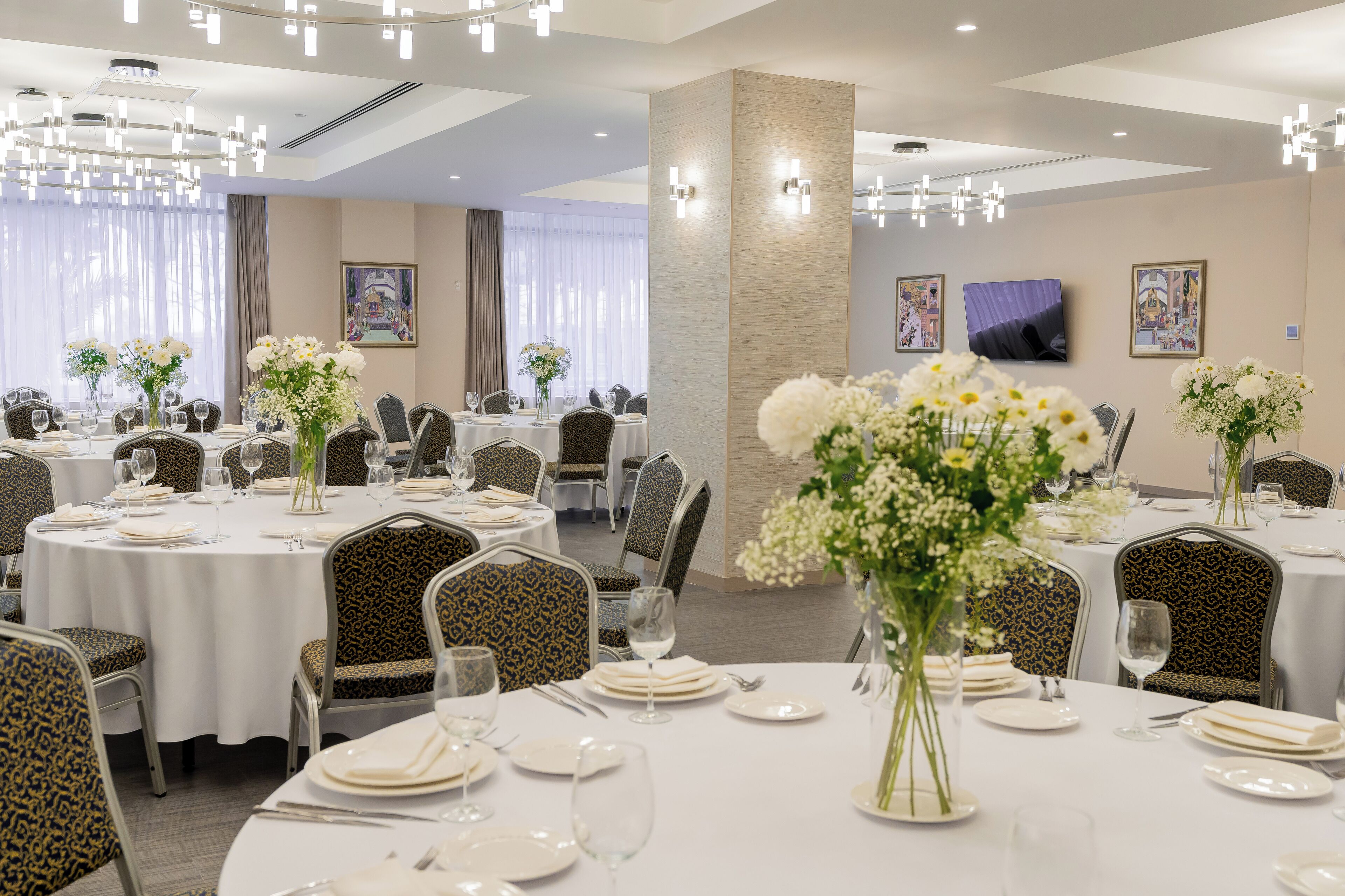 A hotel dining area with round tables, chairs, and floral centerpieces.