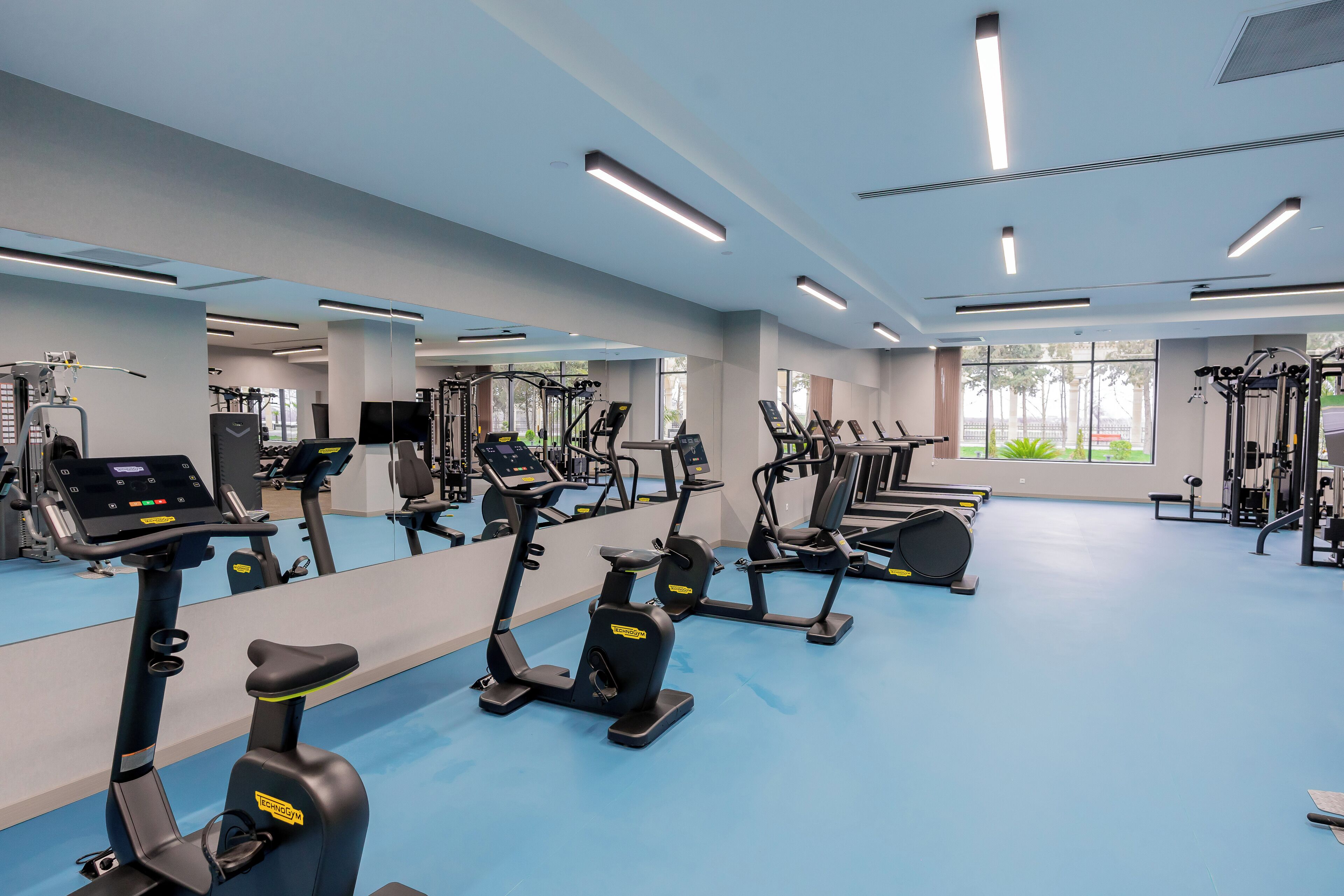 A gym with multiple exercise machines, large windows, and a blue floor.