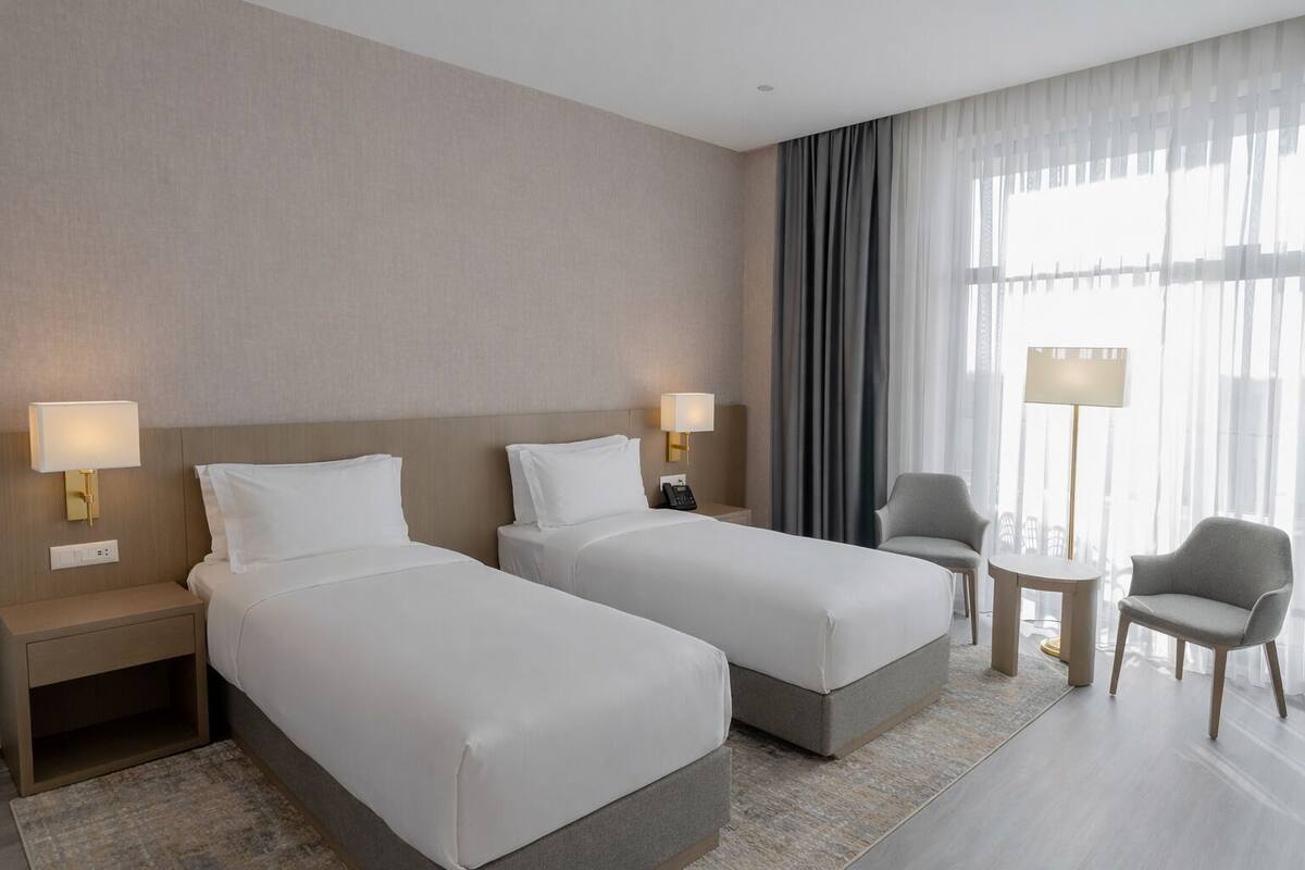 Een hotelkamer met twee bedden, een stoel, een tafeltje en een lamp.