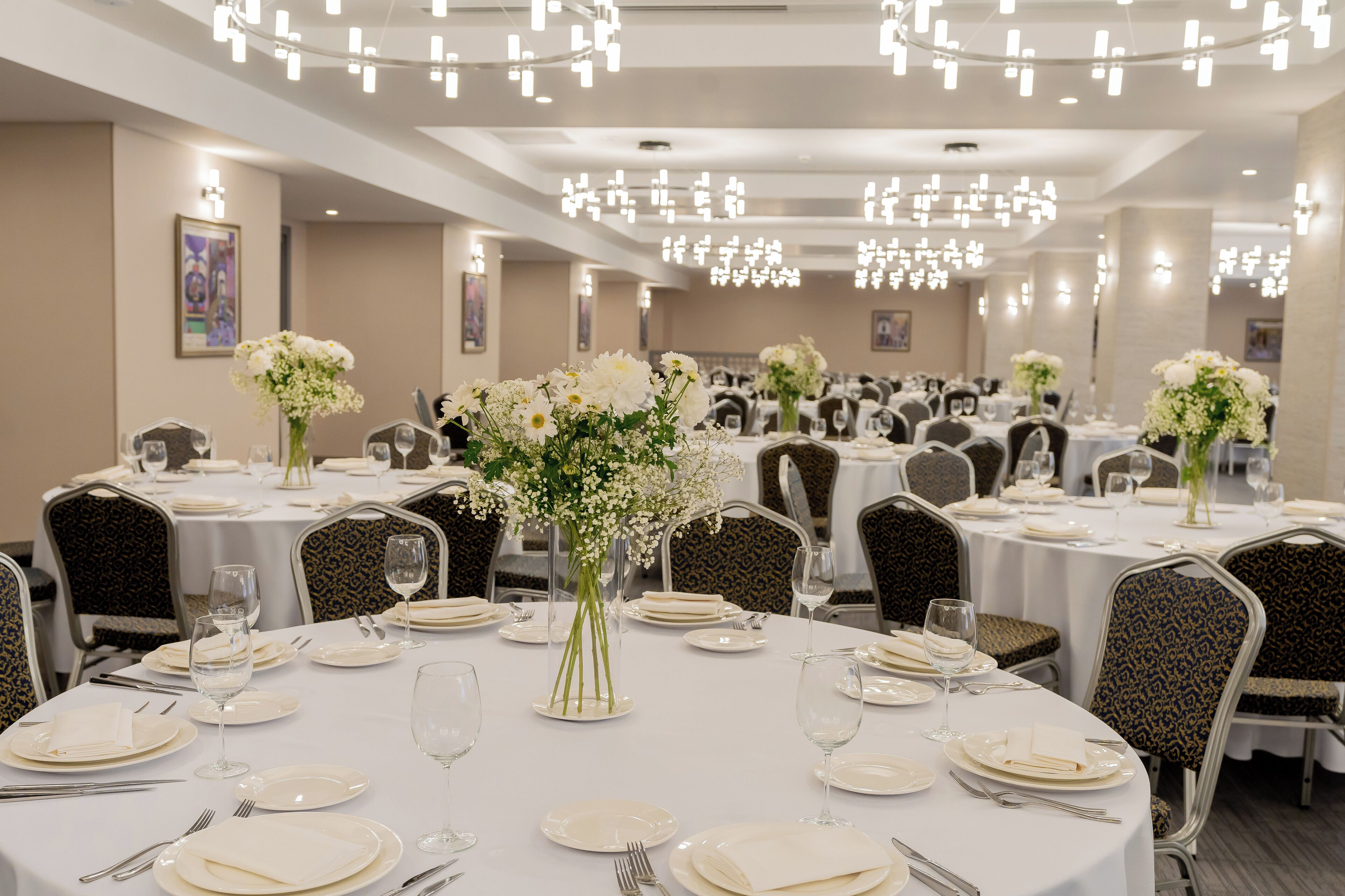 A banquet hall with round tables, chairs, and floral centerpieces.