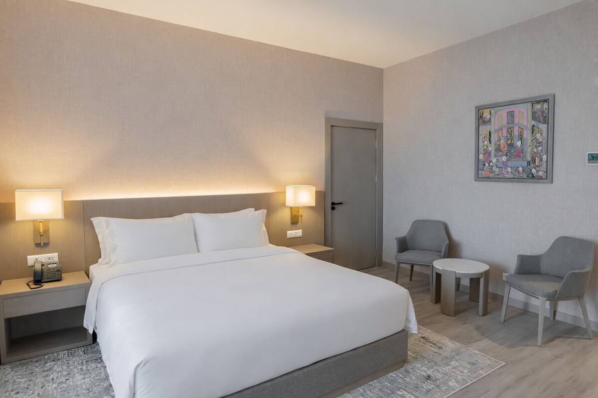 Een hotelkamer met een bed, twee nachtkastjes, een stoel, een klein tafeltje en een deur.