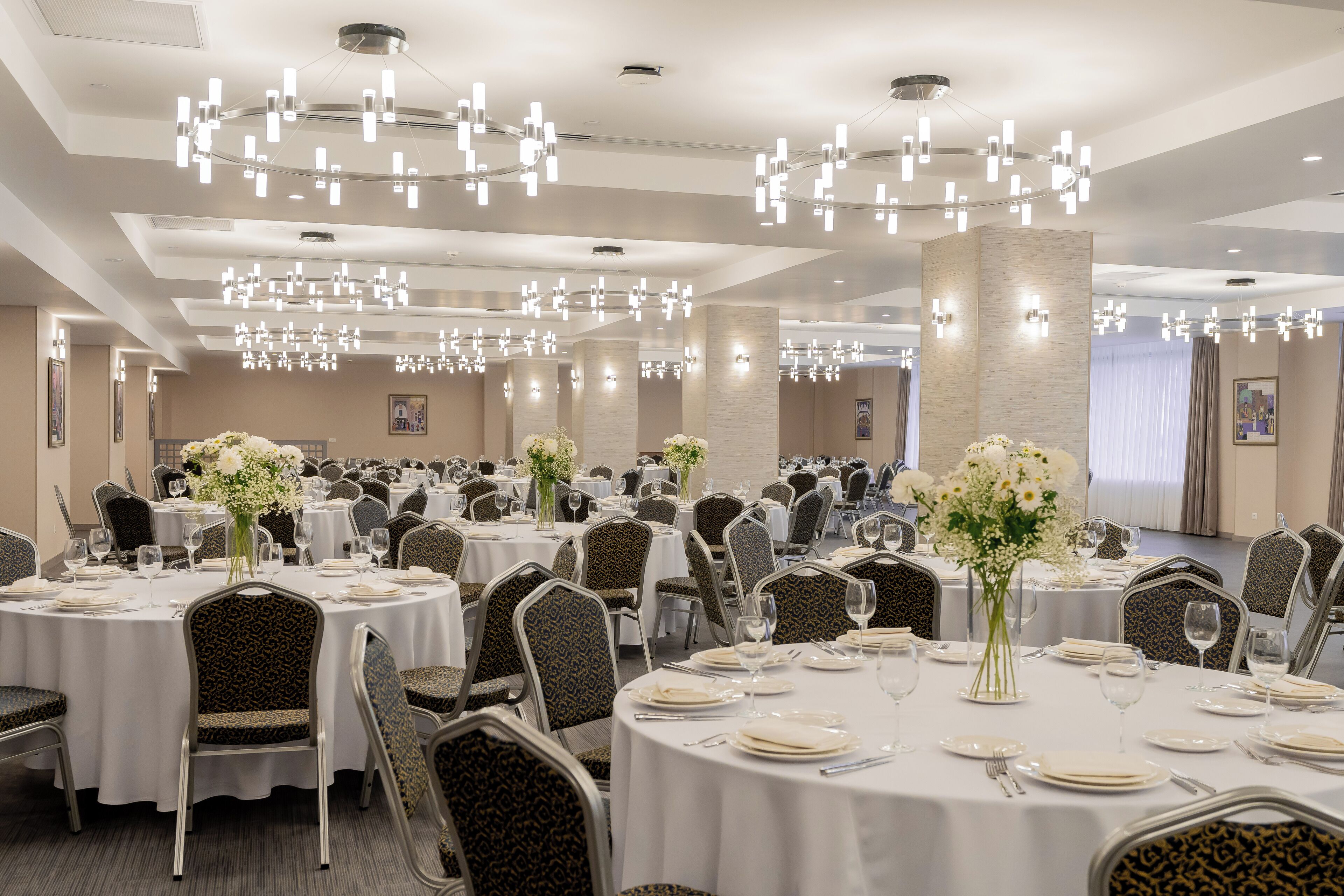 A banquet hall with round tables, chairs, and chandeliers.