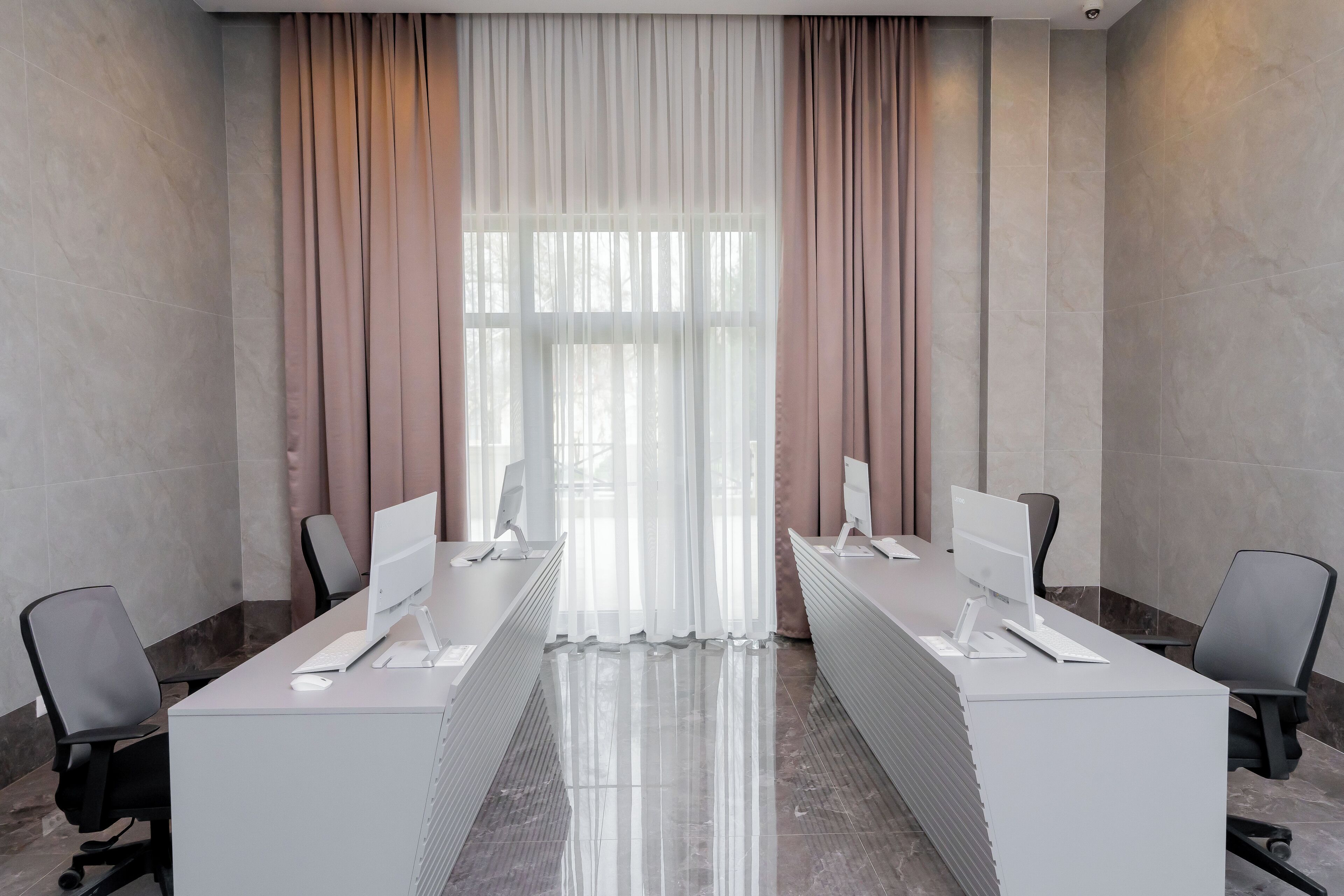 A conference room with two desks, each with a computer and keyboard, chairs, and a large window with curtains.