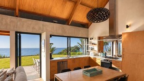 Une cuisine moderne avec vue sur l’océan, des meubles en bois et un coin repas comprenant une table et des chaises.