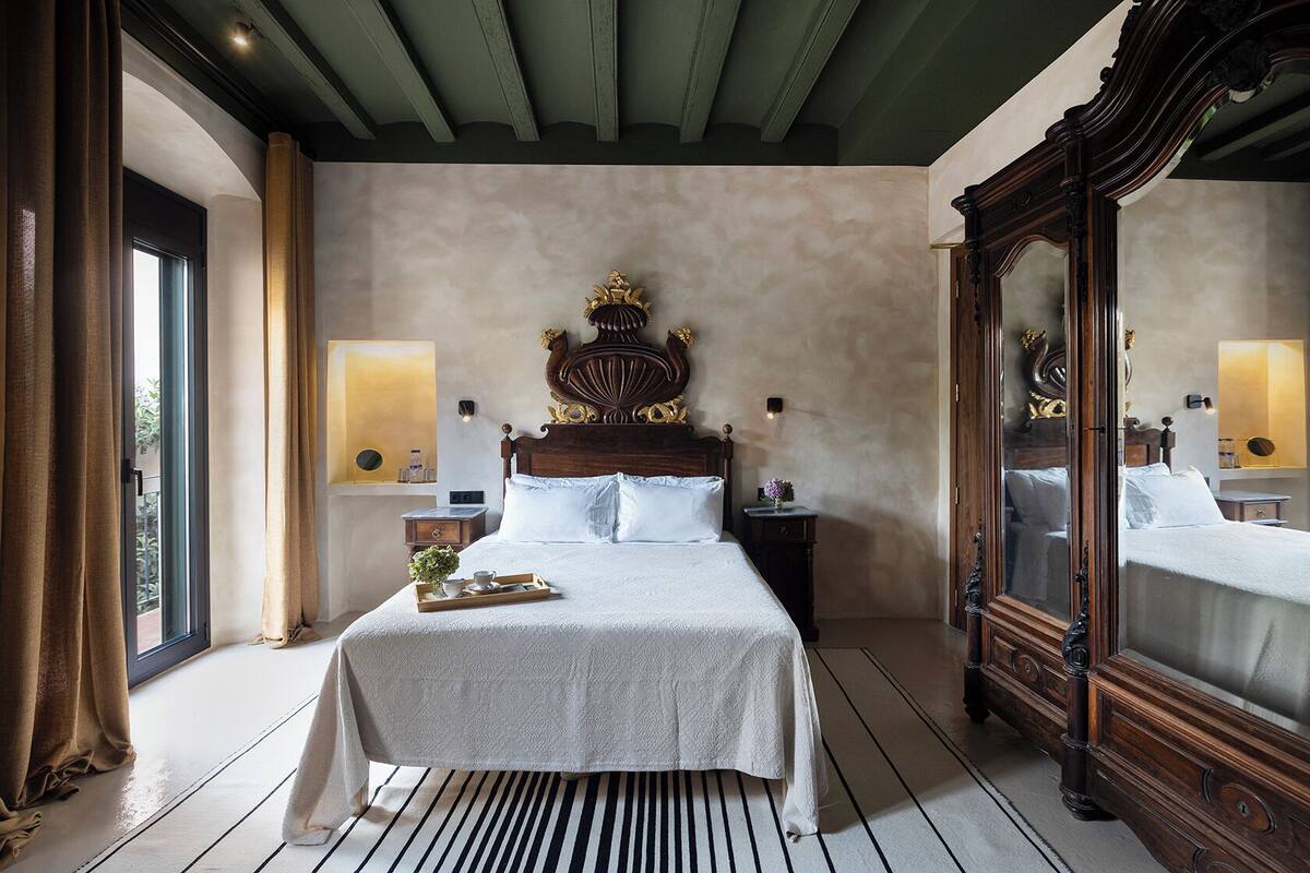 Een slaapkamer met een groot bed, een houten hoofdbord, een nachtkastje, een dressoir en een grote spiegel.