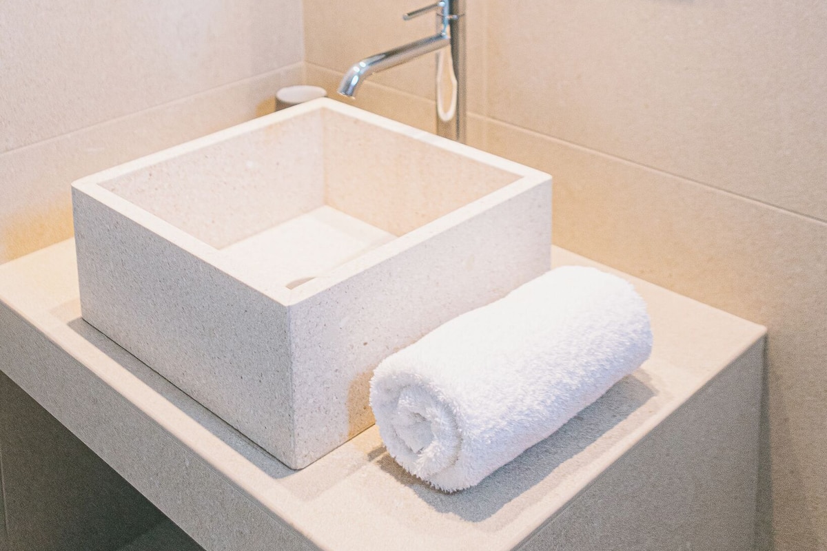 A bathroom with a white rectangular sink, a silver faucet, and a white towel on a beige countertop.