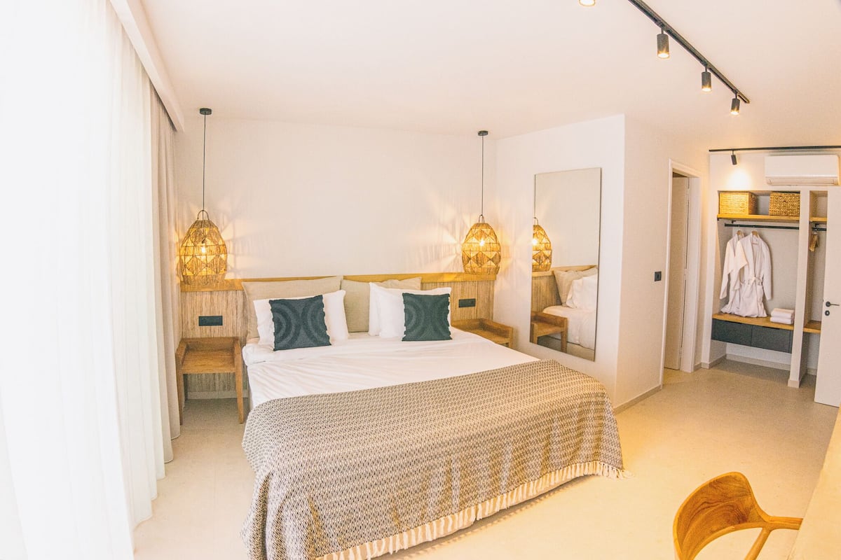 A modern hotel bedroom with a large bed, bedside lamps, a mirror, and a walk-in closet.