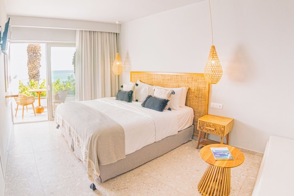 Una habitación de hotel con una cama grande, una mesita de noche de madera, otra mesita redonda de madera y vistas al exterior.