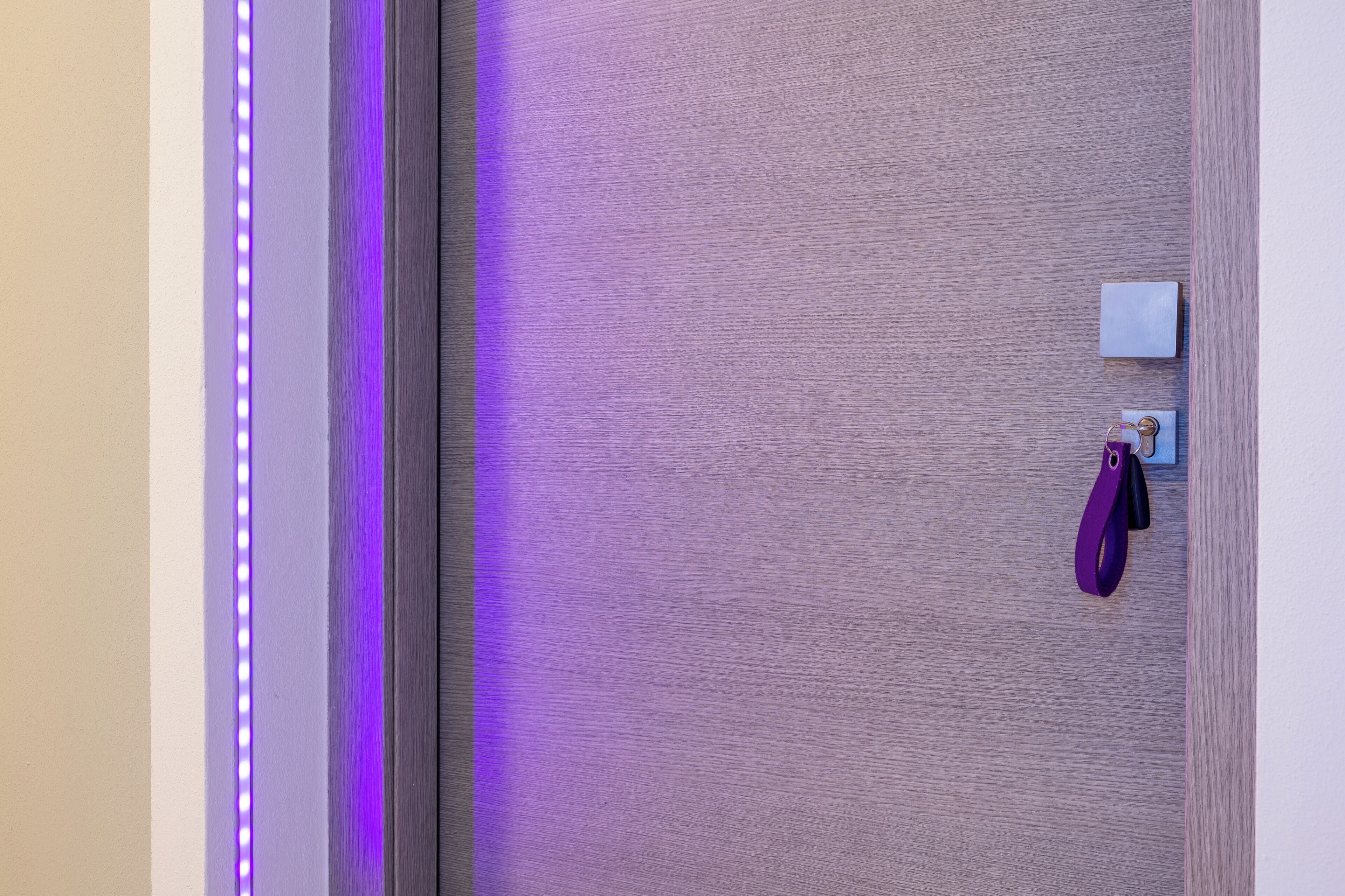 A door with a purple LED light strip, a white object on the wall, and a purple bag hanging on a hook.