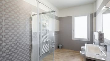 A modern bathroom with a glass shower enclosure, a toilet, and a sink with a mirror above it.